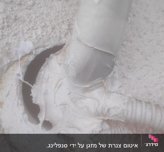 צינור לבן מחובר לקיר עם חומר איטום